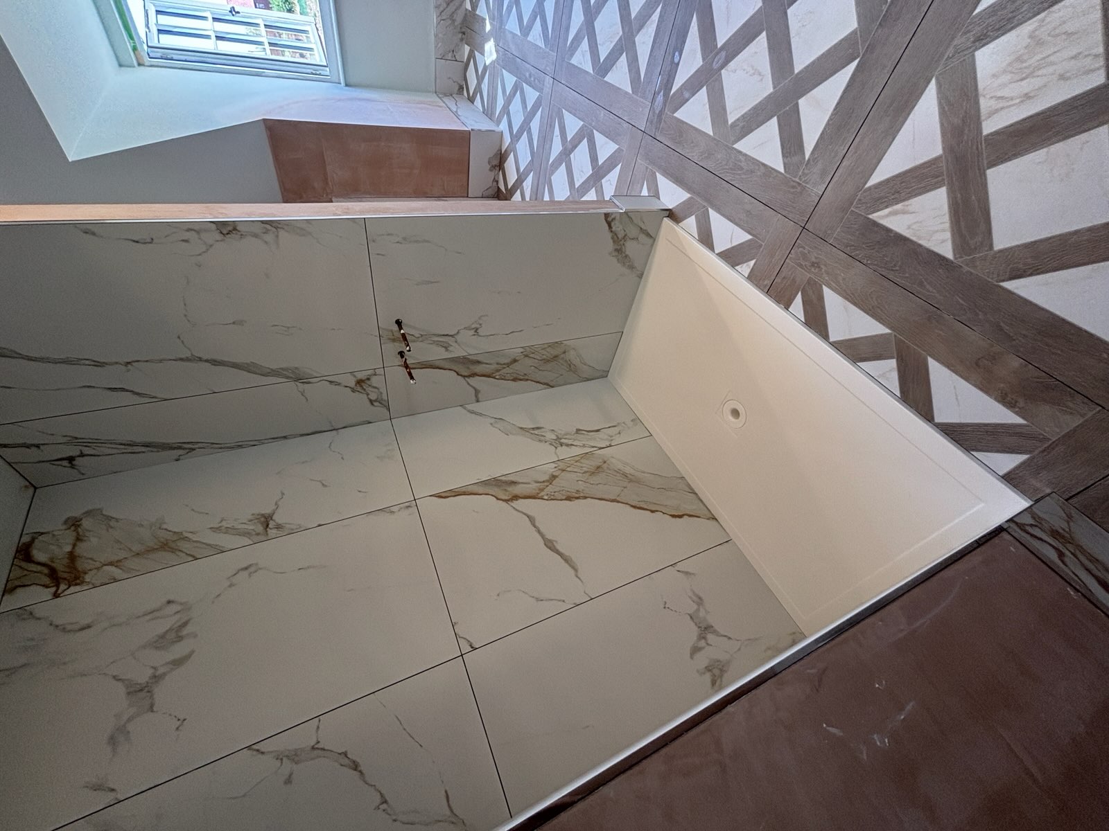 Walk-in shower tray with large marble-effect wall tiles and patterned floor