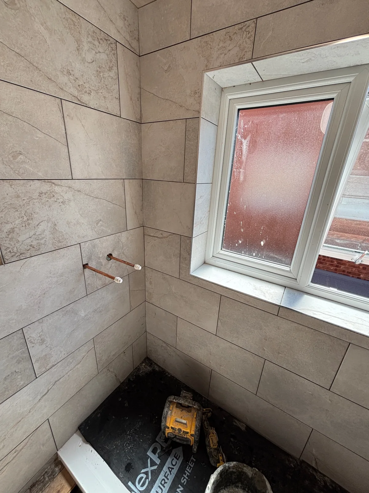 Stone-effect bathroom wall tiles fitted around a window during renovation work