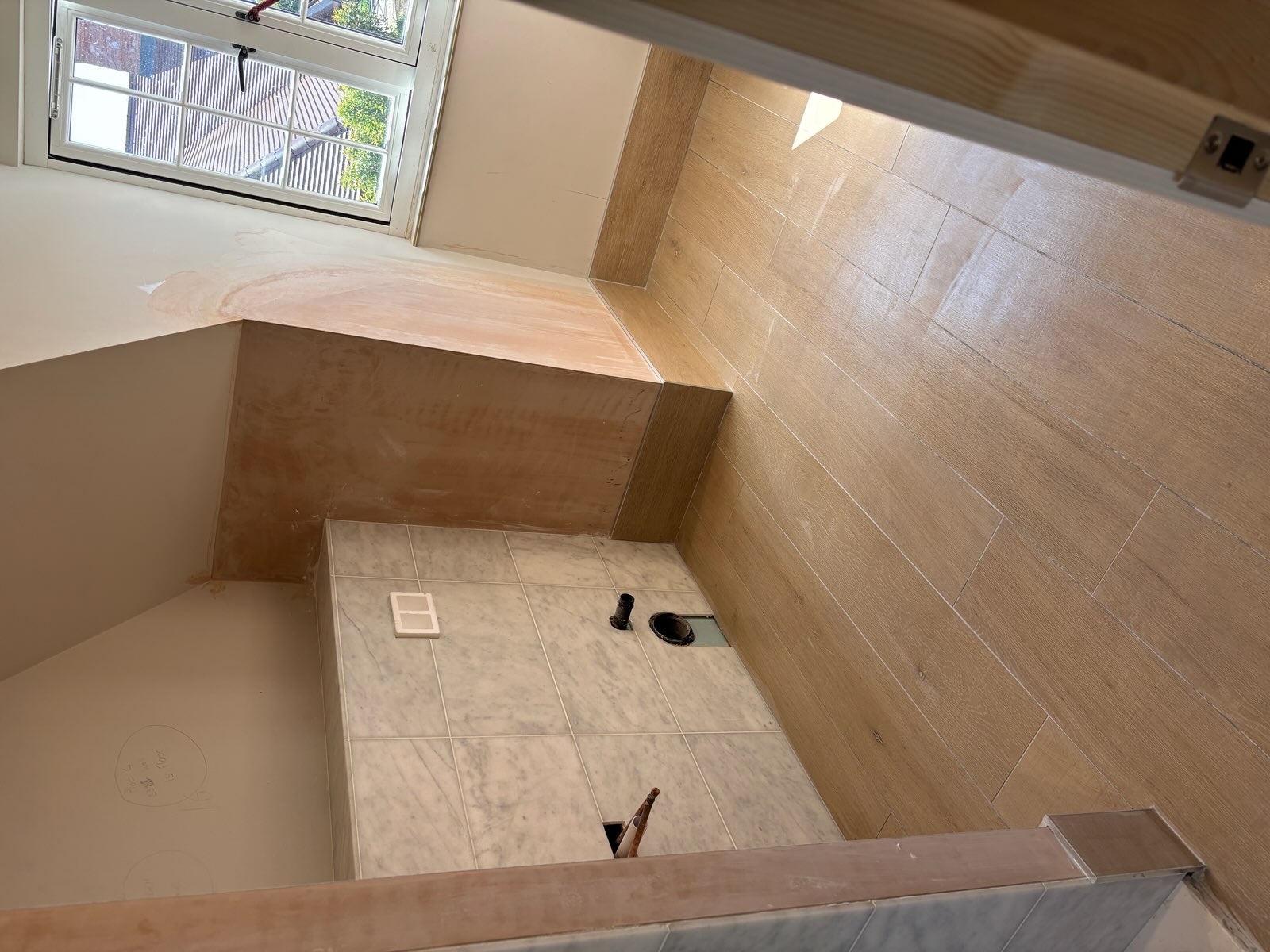 Wood-effect floor tiles and marble-effect wall tiling in a light bathroom